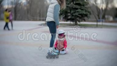 妈妈和女儿<strong>骑</strong>着溜冰鞋。 女孩学习溜冰，摔倒。 妈妈教女儿<strong>骑</strong>车