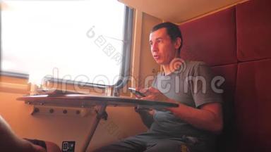 男人坐在<strong>火车车厢</strong>里，手里拿着智能手机铁路，喝着咖啡和茶的生活方式。 慢动作