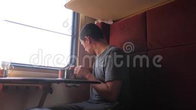 男人坐在火车车厢里，手里拿着咖啡和茶。 慢动作视频。 男人在喝茶
