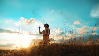 女孩在日落时双手交叉祈祷剪影。 女人的生活方式跪着祈祷。 慢动作视频。 女孩