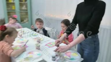 孩子们，男孩和女孩在教室里围着桌子坐在一起画画。 与他们在一起的是他们的年轻