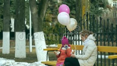 一个漂亮的女孩和她的妈妈坐在公园的长凳上，吃着美味的甜点，喝着热水瓶里的茶