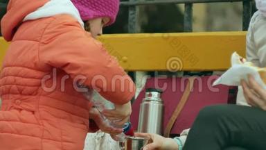 一个漂亮的女孩和她的妈妈坐在公园的长凳上，吃着美味的甜点，<strong>喝</strong>着<strong>热水</strong>瓶里的茶