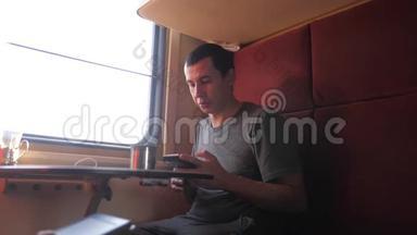 男人坐在火车车厢里，拿着智能手机，喝着咖啡和茶。 慢动作视频。 男人