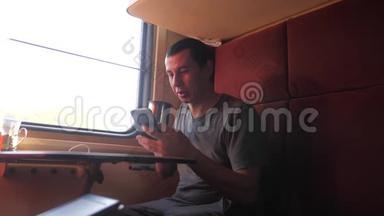 男人坐在火车车厢上，拿着智能手机，喝着生活方式、咖啡和茶。 慢动作