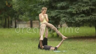 漂亮的一对练习杂技瑜伽。 年轻的瑜伽教练在绿草如茵的城市公园练习。 两次成功