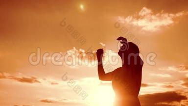 女人跪着祈祷。 女孩在日落时双手交叉在生活方式祈祷剪影中。 慢动作视频。 女孩