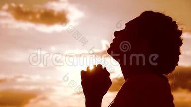 女孩祈祷。 女孩在日落时双手交叉祈祷剪影。 慢动作视频。 女孩双手合拢