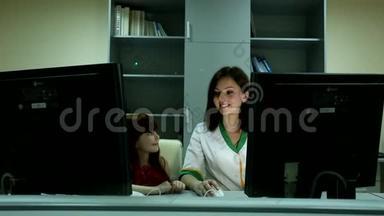 小可爱的女孩看着微笑，年轻迷人的黑发女人医生背后两台电脑显示器商务办公室