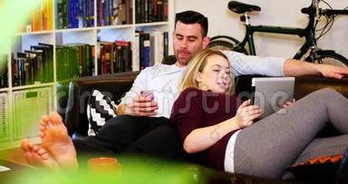 沙发上用手机和数码平板电脑的情侣