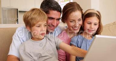 幸福的年轻家庭一起坐在沙发上用笔记本电脑