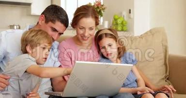 幸福的年轻家庭一<strong>起坐</strong>在沙发上用笔记本电脑