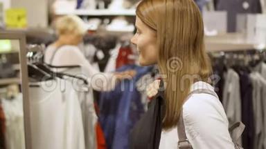 年轻女子在<strong>商场</strong>购物。 站在货架附近，衣服选择夹克。 把蓝色外套捡起来