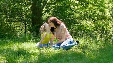 幸福的<strong>一家人</strong>坐在公园的绿草上。 小<strong>女儿</strong>在户外拥抱和亲吻妈妈