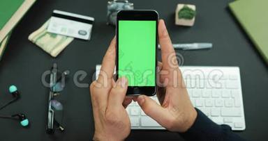男人拿着一个绿色<strong>屏幕</strong>的黑色智能手机在工作桌上<strong>滚动</strong>一些东西