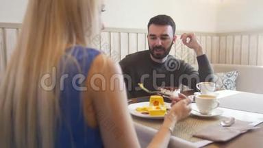 年轻的白种人男人在女人面前试着在咖啡馆吃甜点