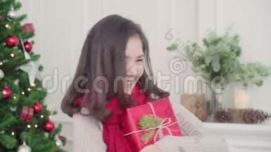 圣诞<strong>佳节</strong>，快乐的年轻亚洲女人在家的客厅里，捧着圣诞礼物微笑着拍照。