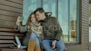 在一个坐在长凳上的春天公园里，年轻的女人和男人在电话里自拍，<strong>喝</strong>着<strong>热水</strong>瓶里的茶
