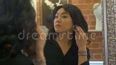 一位亚洲妇女在珠宝店试戴耳环时在镜子上的倒影