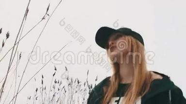 年轻漂亮的金发女孩，穿着黑色夹克和帽子，站在芦苇丛里