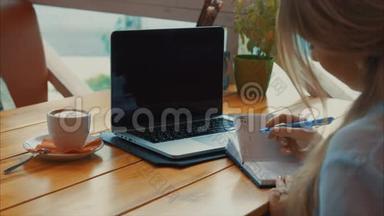 女商人在笔记本上写一支笔，看着笔记本电脑