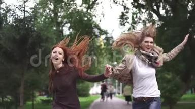 朋友们兴高采烈地穿过夏天的公园，牵着手。 两个红色的女朋友跳着，玩得开心，玩得开心