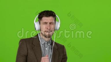 男人通过耳机听音乐，<strong>跳舞和唱歌</strong>。 绿色屏幕。 慢动作