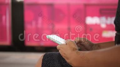 年轻女子坐在地铁车站的长凳上，用手机发短信。 4K.