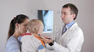 一位年轻的男医生用听诊器给孩子玩。 这个男孩在他母亲`<strong>怀里</strong>。