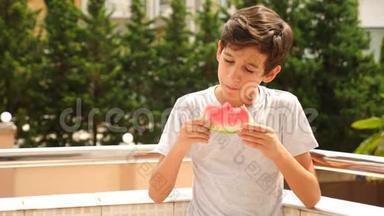 男孩少年在外面吃西瓜，背景是绿色和天空。 慢动作。