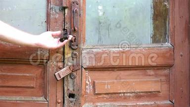 一个人`一扇破旧的旧木门的铁门把手，用手检查紧闭的门锁