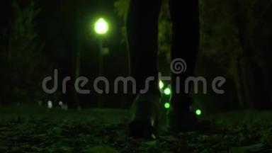 女孩穿着运动鞋走在秋天落叶的夜晚，浅浅的焦点。 公园小巷绿波克灯。 4K视频