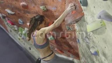 年轻女子攀岩者正在室内攀岩健身房攀岩。 苗条漂亮的女人做一些艰难的动作