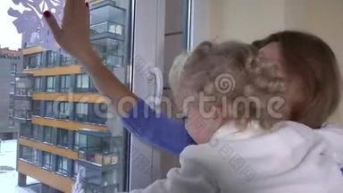 女人和小女孩把纸雪花贴在窗户上。 妈妈带着孩子玩得开心