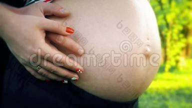 双手抚摸怀孕的肚子。 丈夫`手抚摸着怀孕妻子的腹部。 柔和的夕阳照亮了