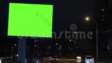 有绿色屏幕的广告牌，位于一条繁忙的街道上。 汽车在晚上移动。
