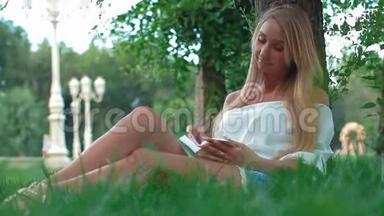 美丽的年轻女子肖像，在公园的一棵树下看书。