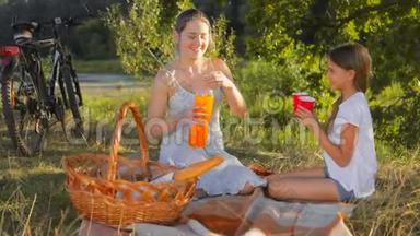 快乐的年轻妈妈和女儿<strong>坐在树下</strong>喝橙汁
