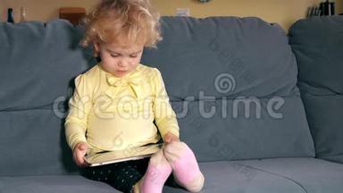 可爱的小女孩用平板电脑坐在沙发上，用手拿电脑