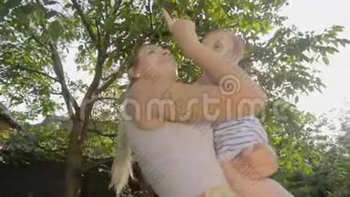 快乐的年轻母亲把她的小儿子高高地抱在果园里快乐的年轻女子在果园里把她的小儿子抱在树下