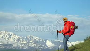 旅行者的女人用棍子爬上山坡进行<strong>追踪</strong>。 红色背包。 用于<strong>追踪</strong>的棍子。
