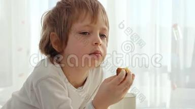 男孩在现代厨房吃早餐。 男孩吃带牛奶的饼干。 厨房里的白色桌子。 碗在桌子上。