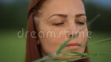晚上，一个红发的年轻美女站在一片绿麦子的田野里，把麦穗放在她的地里
