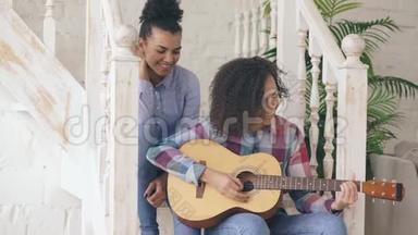 两个巴西卷发女孩坐在楼梯上练习弹<strong>吉他</strong>。 朋友们玩得开心，唱歌