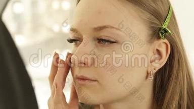 专业化妆师将化妆霜涂在更衣室的问题皮肤年轻女士身上。 化妆女贴身化妆
