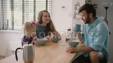 年轻漂亮的三口之家正在厨房的餐桌上吃早餐，笑着。 慢动作，斯蒂达康射中