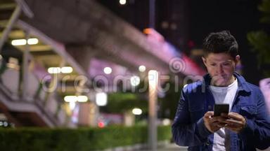 西班牙裔男子在夜间探索城市街道时使用电话