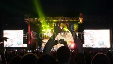 人们在摇滚音乐节上双手跳起来，舞台上灯火辉煌，夜间摇滚音乐会上灯火辉煌
