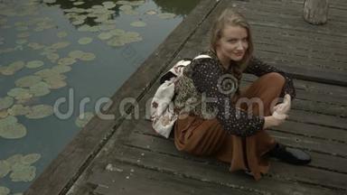 年轻女子坐在木墩上的湖边。