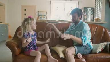 一位年轻的父亲和他可爱快乐的小女儿正坐在沙发上互相给予对方高昂的生活。 慢动作